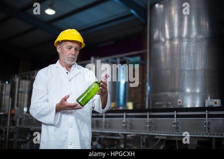 Attento operaio di fabbrica esaminando una bottiglia in fabbrica Foto Stock