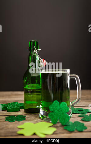 Boccale di birra verde, bottiglia di birra e trifogli per il giorno di San Patrizio sulla tavola di legno Foto Stock