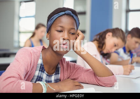 Riflessivo schoolgirl seduta in Aula a scuola Foto Stock