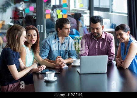 Sorridendo gli imprenditori aventi la discussione su computer portatile in ufficio Foto Stock