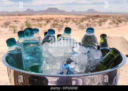 Bottiglie di acqua e birra in una ciotola di acciaio inossidabile con ghiaccio per tenerli fresco. Nella foto durante una calda giornata estiva Doro Nawas Camp, Damaraland, Namibia. Foto Stock