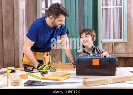 Figlio aiutando il padre lavora con tavole di legno sul portico Foto Stock