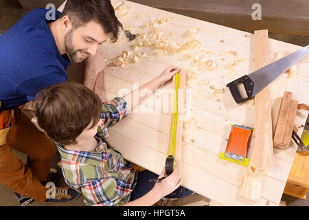 Padre Felice guardando al figlio la misurazione asse di legno con il metro a nastro Foto Stock