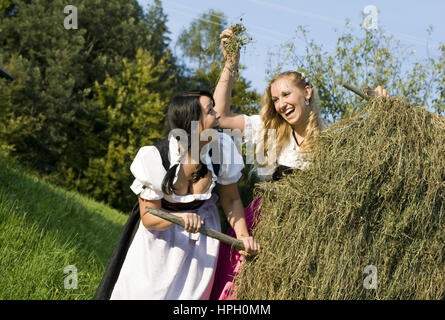 Modello rilasciato , Zwei junge Frauen im Dirndl bei der Heuarbeit - donne in dirndl fare il fieno raccolto Foto Stock
