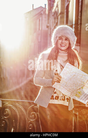 Venezia. Itinerario Insolito. sorridente alla moda donna turistica nel cappello di pelliccia a Venezia, Italia in inverno con mappa Foto Stock