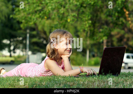 Bambina giacente su erba con il computer portatile Foto Stock