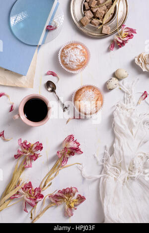 Tazza da caffè, tortine di rosa fiori di tulipano e libro bianco sul tavolo rustico da sopra, prima colazione sulle madri di giorno o Giorno della donna. Foto Stock
