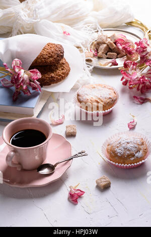 La prima colazione - biscotti di avena, vaniglia muffin con glassa di zucchero, caffè nero. Close-up, tavolo bianco, la luce del mattino Foto Stock