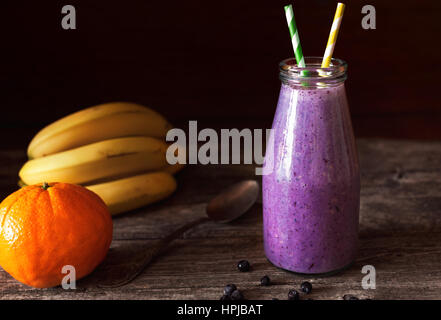 Fresco Frullato viola in una bottiglia di vetro realizzato da banane e mirtilli. Profondità di campo Foto Stock