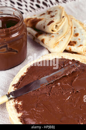 Deliziose frittelle con la nutella cioccolato da spalmare la prima colazione. Spalmatura a coltello crema di cioccolato su una crêpe Foto Stock