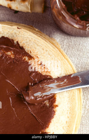 Deliziose frittelle dolci con la nutella cioccolato da spalmare. Coltello dado spreading crema su una crêpe. Profondità di campo Foto Stock