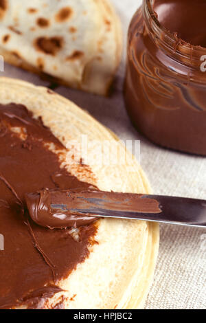 Nutriente e gustosa colazione crepes con la nutella nocciola cioccolato da spalmare. Spalmatura a coltello nutella su pancake. Profondità di campo Foto Stock