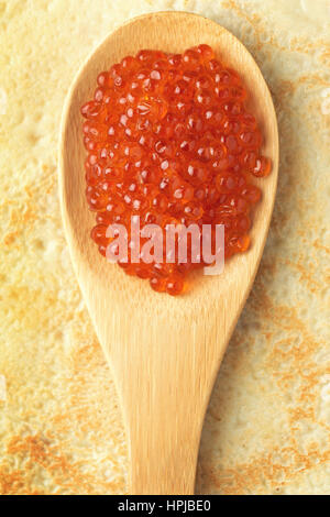 Caviale rosso sul cucchiaio di legno su sfondo pancake. Il russo di delicatezza. Cibo tradizionale per Maslenitsa Foto Stock