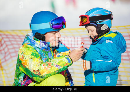 Padre e figlio in sci outfits giocando con il giocattolo in appoggio sulla pista da sci Foto Stock