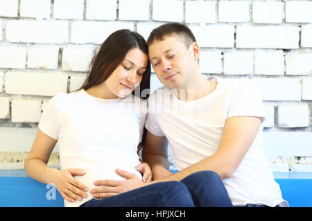 Giovane donna incinta e suo marito con sveglia rossa Foto Stock