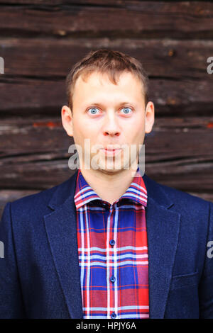 Sorpreso uomo in giacca blu e camicia a scacchi su uno sfondo di legno Foto Stock