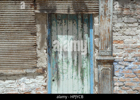 Una porta di legno consumata con vernice blu e verde scrostata, inserita in un muro rustico di mattoni e stucco, L'Avana, Cuba. Foto Stock