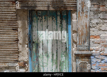 Una porta di legno consumata con vernice blu e verde scrostata, inserita in un muro rustico di mattoni e stucco, L'Avana, Cuba. Foto Stock
