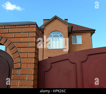 La parte superiore della casa di abitazione parete anteriore di mattoni rossi con timpani e finestra ad arco dietro il recinto di mattoni rossi con gate metallici. Foto Stock