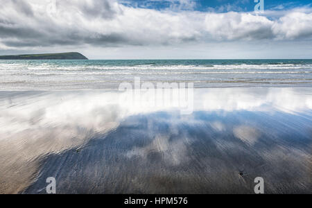 Sabbia bagnata su una spiaggia deserta che riflette la luce nuvoloso cielo blu Foto Stock