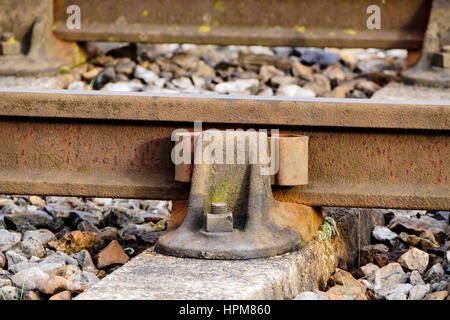 Un vecchio stile presieduto il binario ferroviario con paratia rampa e traversine di cemento con pietre di zavorra. Foto Stock