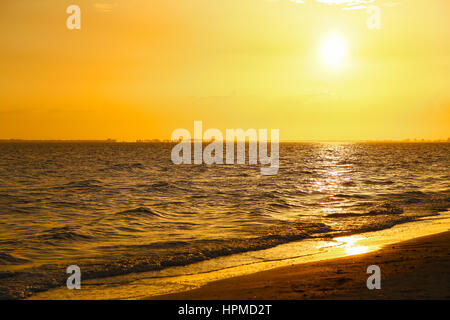 Il sole che tramonta su un arancio luminoso cielo sopra il Golfo del Messico in Fort Myers Beach con la spiaggia in primo piano. Foto Stock