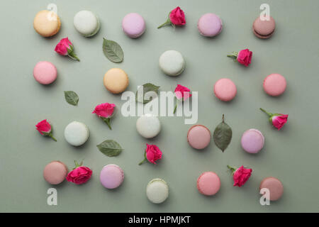 Macarons piana withroses laici e foglie su sfondo verde. Vista superiore Foto Stock