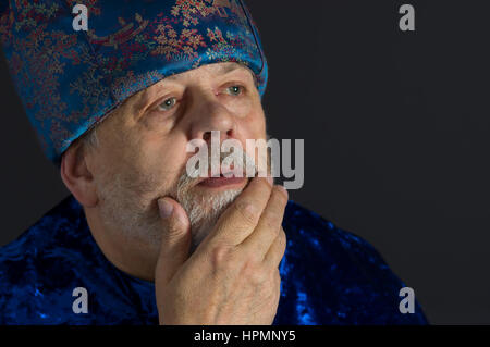 Ritratto di meditazione senior uomo in blu i vestiti orientali contro uno sfondo scuro Foto Stock