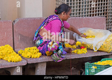 La donna non identificato in un Ahmedabad backstreet fare ghirlande di fiori di tagete per la vendita di adoratori come offerte in un vicino tempio indù Foto Stock