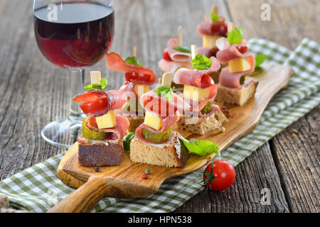 Sudtirolese antipasti: fresco imburrato pane rustico con pancetta affumicata, abbondante formaggio di montagna, sottaceti e pomodori, le foglie di basilico sulla parte superiore Foto Stock