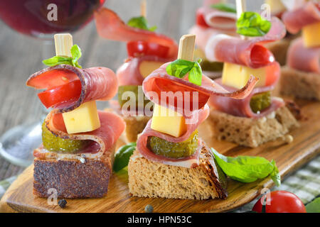 Sudtirolese antipasti: fresco imburrato pane rustico con pancetta affumicata, abbondante formaggio di montagna, sottaceti e pomodori, le foglie di basilico sulla parte superiore Foto Stock
