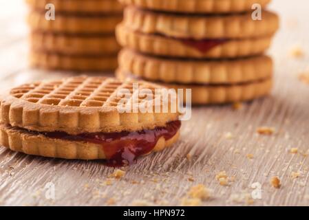 Foto orizzontale di diverse pile di golden biscotti. I biscotti sono a bacca rossa marmellate fatte in casa. I biscotti sono collocati sul bianco luce pannello di legno Foto Stock