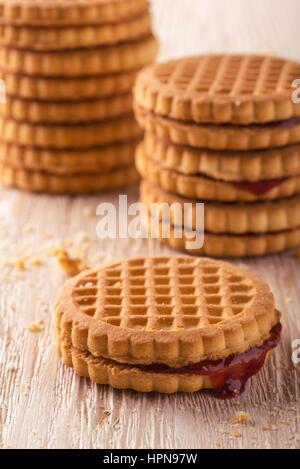 Foto verticale di diverse pile di golden biscotti. I biscotti sono a bacca rossa marmellate fatte in casa. I biscotti sono collocati sulla luce di legno bianco bordo. Foto Stock