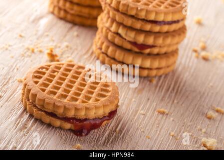 Foto orizzontale di diverse pile di golden biscotti. I biscotti sono a bacca rossa marmellate fatte in casa. I biscotti sono collocati sul bianco luce pannello di legno Foto Stock