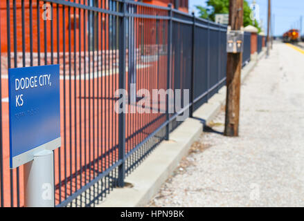 DODGE CITY, Stati Uniti d'America - 17 Maggio 2015: La stazione ferroviaria della città con un cartello indicante Dodge City, anche in Braille. Nella parte posteriore di un treno è approachin Foto Stock