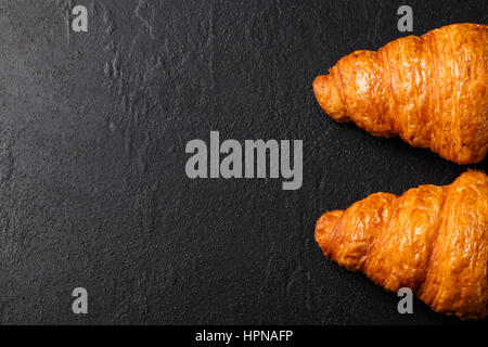 Croissant fresco su un nero ardesia sfondo. Vista dall'alto uno spazio di copia Foto Stock