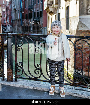 Venezia. Itinerario insolito. A piena lunghezza Ritratto di bambino moderno a Venezia, Italia in inverno mostra pollice in alto Foto Stock