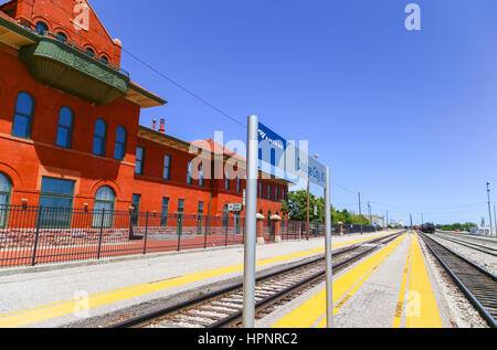 Dodge City, Stati Uniti d'America - 17 Maggio 2015: la stazione Amtrak della città con le piattaforme e le vie e l'edificio storico nonché un moderno segno, nel retro di un Foto Stock