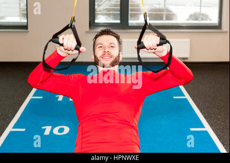 Ricci bianco barbuto uomo sportivo esercitando con cinghie di fitness in palestra Crossfit istruttore presso la palestra facendo Excersise. Uomo Fitness workout sugli anelli. Sport e fitness. Crossfit allenamento Foto Stock