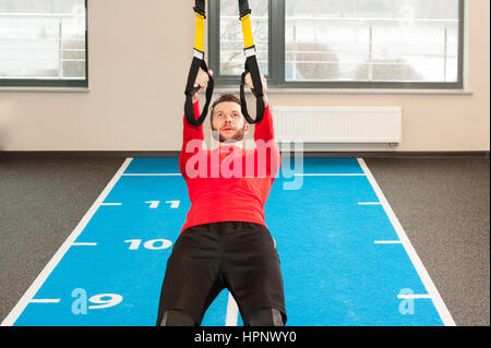 Ricci bianco barbuto uomo sportivo esercitando con cinghie di fitness in palestra Foto Stock