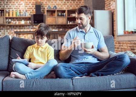 Man aventi la prima colazione durante il figlio facendo i compiti di scuola Foto Stock