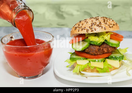 Grande Burger e succo di pomodoro versata nella tazza di vetro. Tazza Foto Stock