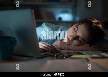 Assonnato esaurito donna che lavorano in ufficio con il suo portatile, è dormire con gli occhi chiusi, lavoro straordinario concetto Foto Stock
