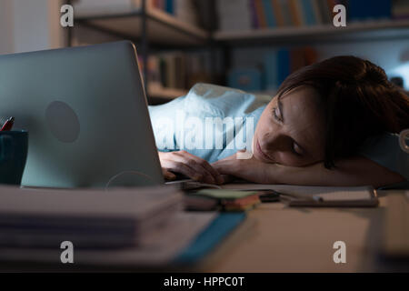 Assonnato esaurito donna che lavorano in ufficio con il suo portatile, è dormire con gli occhi chiusi, lavoro straordinario concetto Foto Stock