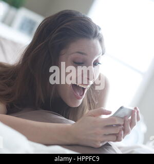 Donna felice a casa la lettura di un messaggio di testo nella sua camera da letto luminose Foto Stock