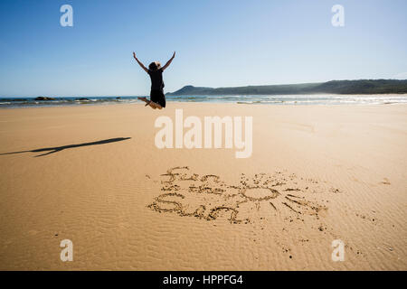 Donna che si tuffa per il divertimento sulla spiaggia sabbiosa, divertimento al sole scritto in sabbia, Croajingolong, Victoria, Australia Foto Stock