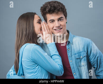 Giovane donna carina whispering segreti nel suo fidanzato l orecchio Foto Stock