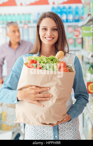 Sorridente giovane donna fare la spesa al supermercato, lei sta tenendo in mano un sacchetto con verdure fresche Foto Stock