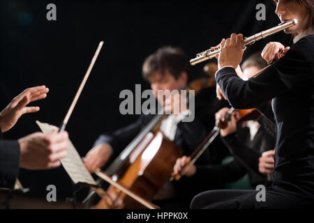 Il conduttore dirigere Symphony orchestra in concerto con il flautista in primo piano. Foto Stock