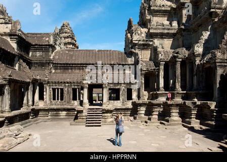 Una vista dall'interno di Angkor Wat complesso di un turistica prendendo fotografie vicino al santuario centrale in una giornata di sole con cielo blu. Foto Stock